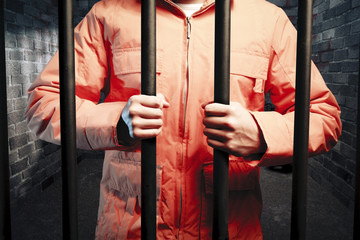 Orange jumpsuit hands gripping bars jail cell brick wall